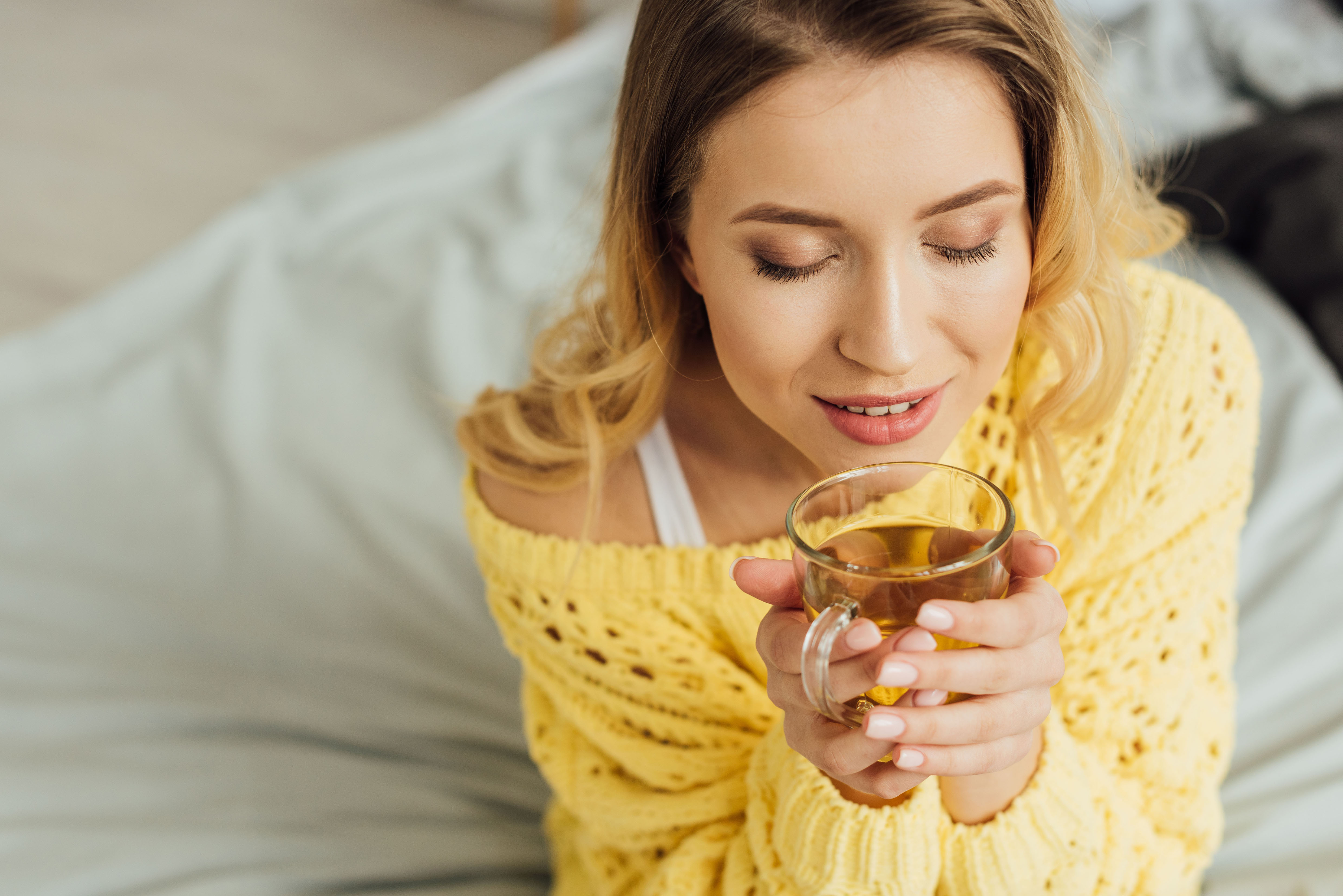 Junge Frau hält eine Tasse Kräutertee mit beiden Händen und schließt die Augen