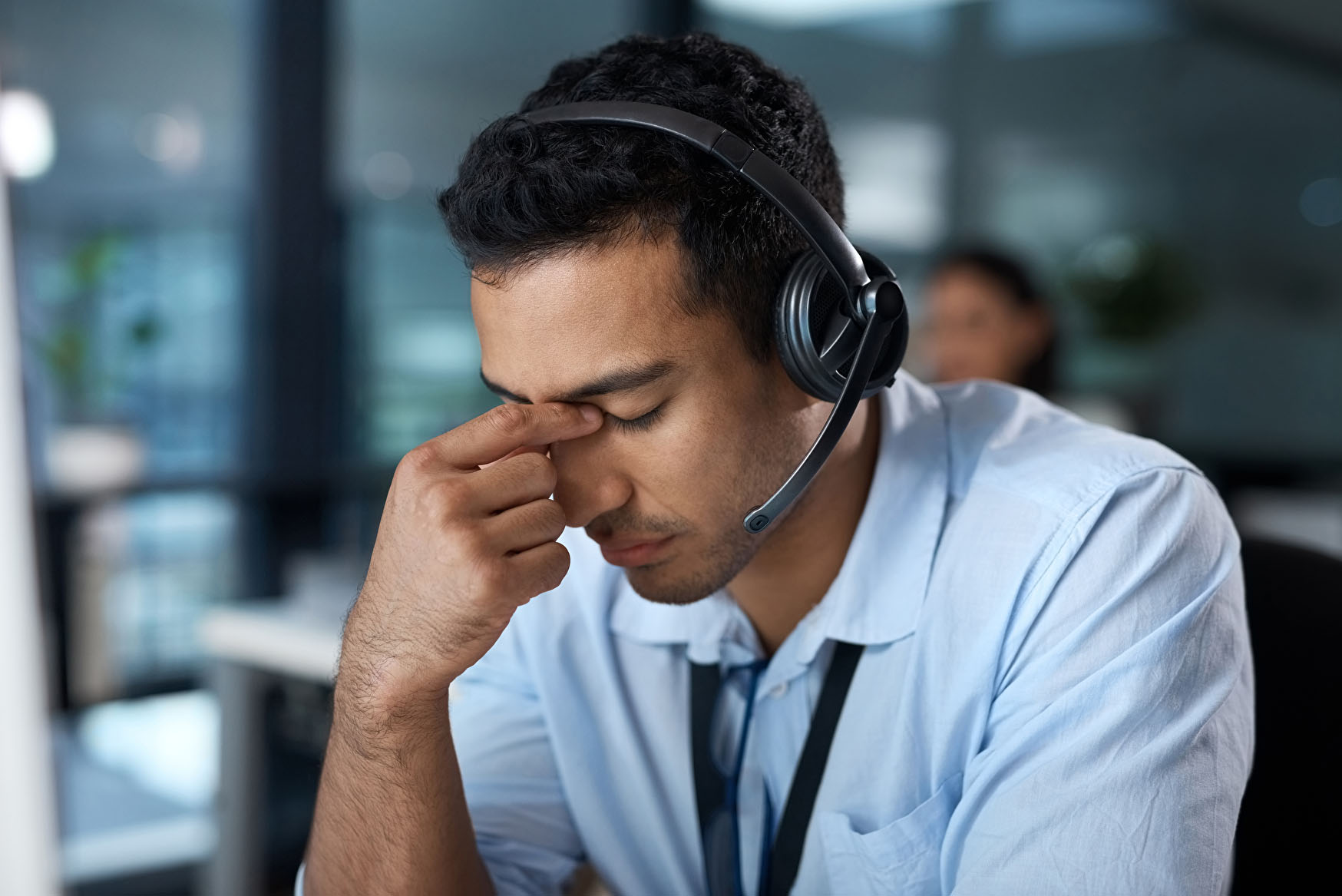Mann im Büro mit Kopfhörern drückt mit den Fingern auf die Nasenwurzel