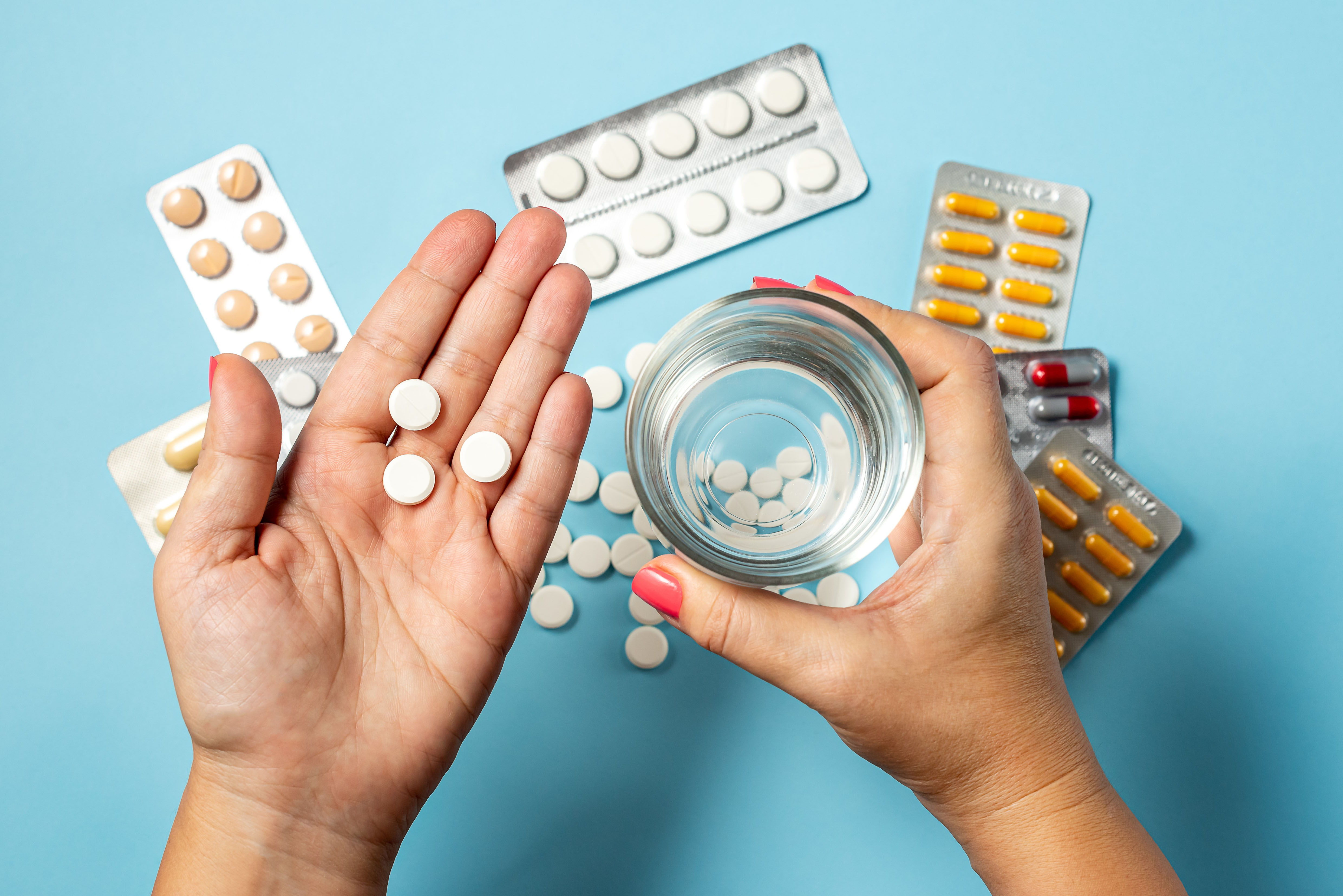Hände mit Tabletten und Wasserglas über Tisch mit vielen Tabletten